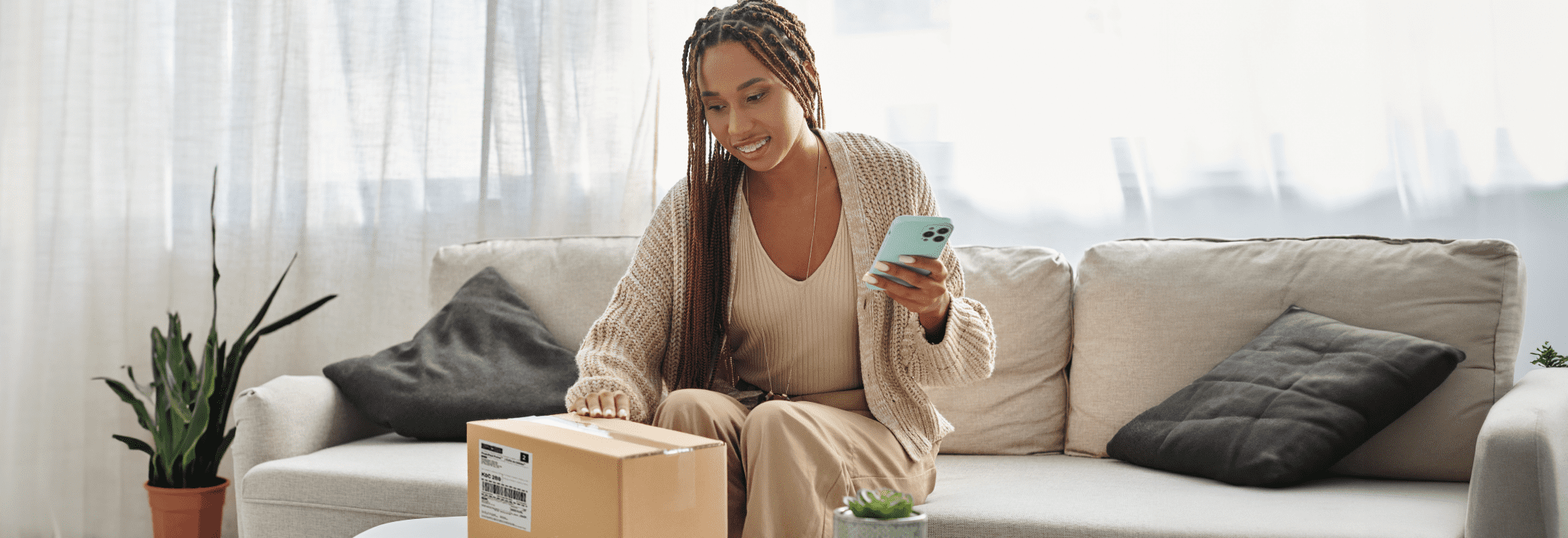 Une femme souriante regarde son téléphone intelligent en tenant un colis.