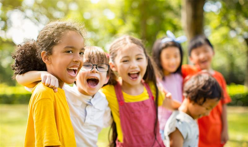 Des enfants souriants sont debout dans une salle de classe, les bras en l’air