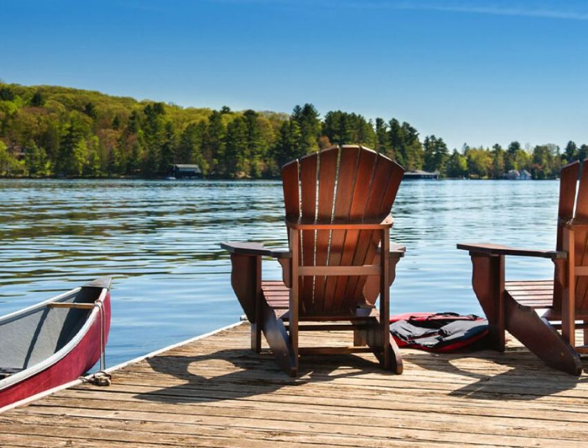 Deux chaises en bois reposent sur un quai au bord d’un lac, à côté d’un canot.