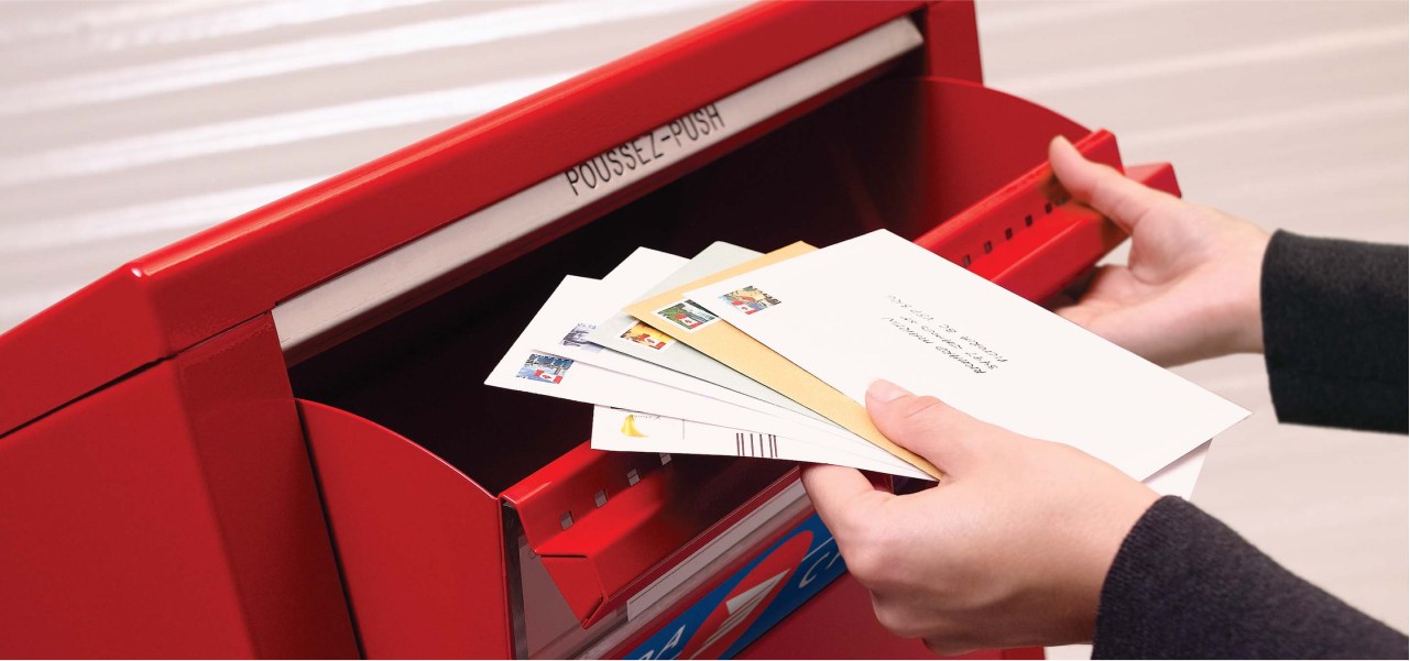 Une pile d’enveloppes prêtes pour l’expédition est placée dans une boîte aux lettres publique de Postes Canada