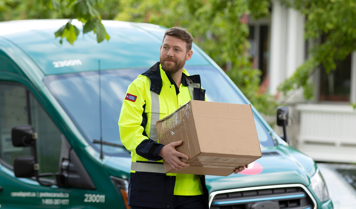 Un facteur en blouson jaune vif transporte deux colis. Une fourgonnette hybride de Postes Canada est stationnée derrière lui.